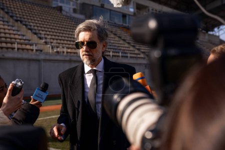 Interview of football team director at press conference for TV news. Organization representative answering questions and giving interview outside a soccer stadium. Journalists crowd on press campaign.