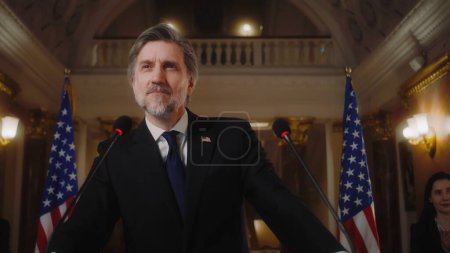 Photo for American republican politician during press conference in the White House. Confident US minister or congressman smiles, poses for cameras after political speech. USA flags in background. Slow motion. - Royalty Free Image