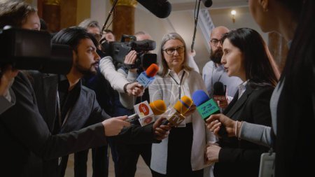 Politician answers press questions and gives interview for television breaking news. Diplomat, consul surrounded by crowd of journalists. Political speech during press conference. State of the nation.