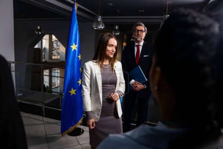 Photo for Positive female Representative of the European Union poses for the cameras and greets journalists. Correspondents take photos and broadcast on TV. EU politician at the beginning of press conference. - Royalty Free Image