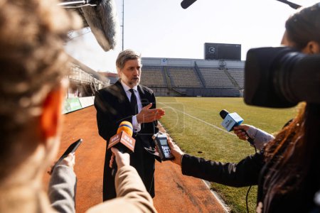 Photo for Interview of private investor at press conference for TV news in soccer stadium. Director of football team answering press questions and giving interview. Inspirational speech during press campaign. - Royalty Free Image