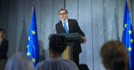 Mature representative of the European Union performs at press conference. Confident politician makes an announcement, delivers campaign speech, gives interview to journalists and media. Election day.