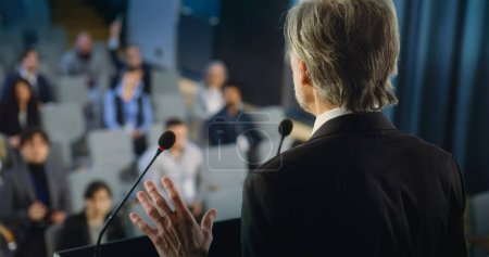 Photo for Back view of politician or activist pronouncing speech during press campaign in the conference hall. Mature organization representative answers questions, gives interview to journalists for media. - Royalty Free Image