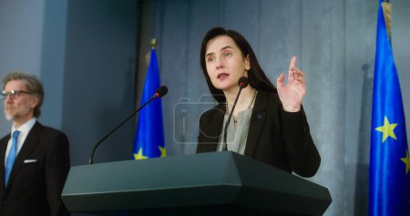 Photo for Female representative of the European Union during press conference. Confident politician pronounces political speech, answers journalists questions, gives interview for media. Backdrop with EU flags. - Royalty Free Image