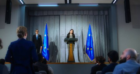 Photo for Female representative of the European Union during press conference. Confident politician makes an announcement, answers journalists questions and gives interview for media. Backdrop with EU flags. - Royalty Free Image