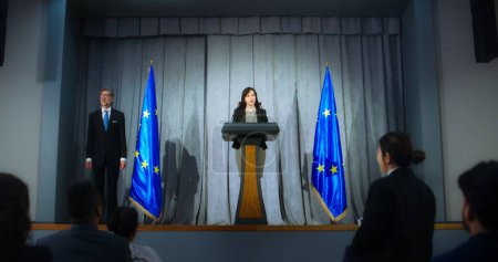Téléchargez les photos : Représentante féminine de l'Union européenne lors de la conférence de presse. Un politicien confiant fait une annonce, répond aux questions des journalistes et donne une interview aux médias. Contexte avec les drapeaux de l'UE. - en image libre de droit