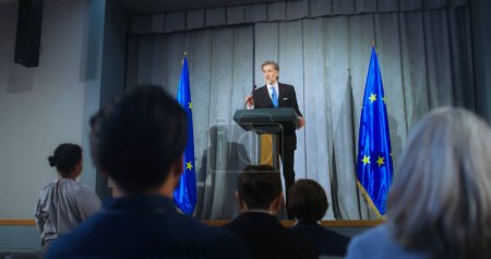 Téléchargez les photos : Représentant mature de l'Union européenne lors de la conférence de presse. Un politicien confiant fait une annonce, répond aux questions des médias et donne une interview. Contexte avec les drapeaux de l'UE. - en image libre de droit