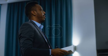 Photo for Multiethnic journalists sit and write answers from organization representative during press campaign in conference room. African-American press worker stands up and asks questions during interview. - Royalty Free Image