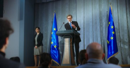 Mature politician comes to tribune, delivers campaign speech, answers journalists questions, gives interview to media. Representative of the European Union performs at press conference. Elections day.