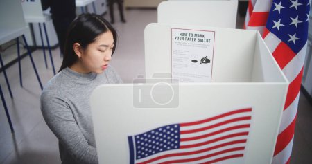 Foto de Votante asiática eligiendo candidato presidencial para votar en cabina de votación en el centro de votación. Ciudadano estadounidense durante el Día Nacional de Elecciones en los Estados Unidos. - Imagen libre de derechos