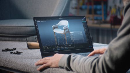 Téléchargez les photos : Creative man utilise des logiciels professionnels pour la création de meubles et la modélisation 3D sur ordinateur portable. Designer crée le modèle 3D numérique de chaise en bois élégant, prépare le projet de menuiserie. - en image libre de droit