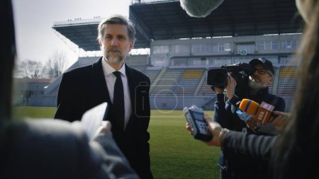 Photo for Private investor crowded by news journalists near soccer field. SEO or director of football team answering press questions and giving interview before match. Inspirational speech on press conference. - Royalty Free Image