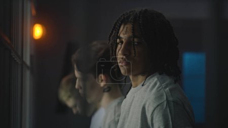 Afroamerikanische Teenager stehen mit kaukasischen Jungen in der Nähe der Gefängniszelle, schauen in die Kamera. Junger Häftling verbüßt Haftstrafe für Verbrechen im Gefängnis. Jugendhaftanstalt oder Justizvollzugsanstalt.