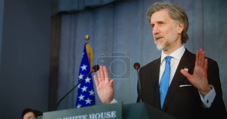 Photo for US presidential candidate pronounces campaign speech from the tribune at press conference in the White House. Politician answers questions, gives interview for media. American flags in the background. - Royalty Free Image