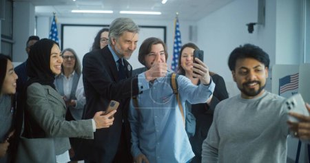 Foto de Ciudadanos estadounidenses multiétnicos felices se toman selfies con candidato presidencial maduro después de votar. Diversas personas con políticos en el centro de votación. Día Nacional de Elecciones en los Estados Unidos. Movimiento lento. - Imagen libre de derechos