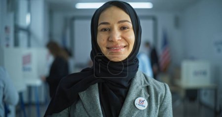 Photo for Portrait of Arabic woman, United States of America elections voter. Woman stands in a modern polling station, poses, smiles and looks at camera. Background with voting booths. Concept of civic duty. - Royalty Free Image
