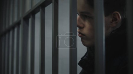 Le gardien enlève les menottes d'un jeune prisonnier debout derrière des barreaux en métal. L'adolescent purge une peine d'emprisonnement dans un établissement correctionnel ou un centre de détention. Détenu coupable dans les cellules de prison. Gros plan.