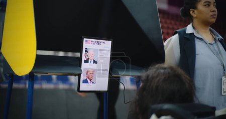 Foto de ZAPORIZHYA, UCRANIA - 15 DE MARZO DE 2024: Votante femenina, mujer con SMA en silla de ruedas vota en cabina de votación en el centro de votación. Ciudadano de los Estados Unidos con discapacidad utiliza tableta para votar. Presidencial - Imagen libre de derechos
