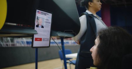 Téléchargez les photos : ZAPORIZHYA, UKRAINE - 15 MARS 2024 : Une femme ayant un handicap physique fait un choix et vote au bureau de vote à l'aide d'un ordinateur tablette. Campagne électorale de Joe Biden affiché sur l'écran de la tablette - en image libre de droit