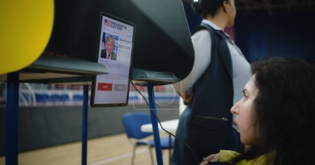 Foto de ZAPORIZHYA, UCRANIA -MARZO 15, 2024: La mujer estadounidense con discapacidad SMA elige, vota en el centro de votación con Tablet PC, lee la campaña electoral de Donald Trump que se muestra en la pantalla de la tableta - Imagen libre de derechos