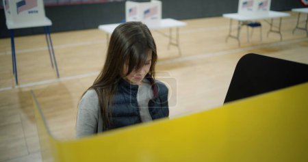 Foto de La mujer caucásica elige y vota en la cabina de votación en el centro de votación, luego se va. Votante femenina, ciudadana estadounidense durante las elecciones presidenciales en los Estados Unidos de América. Deber cívico y democracia. - Imagen libre de derechos