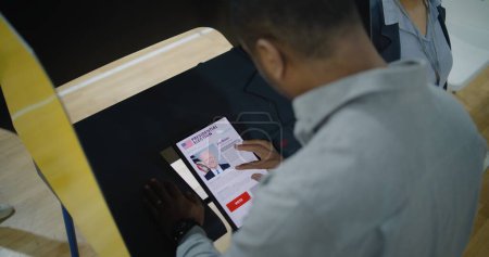 Foto de ZAPORIZHYA, UCRANIA -15 DE MARZO DE 2024: Votante afroamericano hace elección y vota por Joe Biden en la cabina de votación usando tableta. Ciudadano estadounidense durante las elecciones presidenciales en Estados Unidos - Imagen libre de derechos