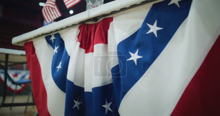 Close up of table for voting registration with American flags standing at polling place. Elections in the United States of America. Presidential race and election coverage. Civic duty and democracy.