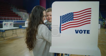 Frau mit Kind an der Hand kommt in die Wahlkabine. Amerikanische Bürger kommen in die Wahllokale, um ihre Stimme abzugeben. Politische Rennen der US-Präsidentschaftskandidaten. Nationaler Wahltag in den Vereinigten Staaten. Dolly erschossen.
