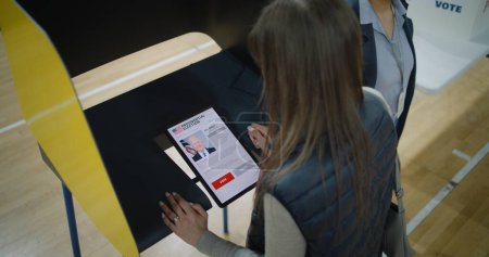 Téléchargez les photos : ZAPORIZHYA, UKRAINE - 15 MARS 2024 : Gros plan sur les électrices qui choisissent et votent pour Joe Biden dans les isoloirs à l'aide d'un ordinateur tablette. Citoyen américain au bureau de vote pendant la présidentielle - en image libre de droit