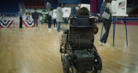 Woman with physical disability in electric wheelchair comes to vote in polling station. American citizens during political races of US presidential candidates. National Election Day in United States.