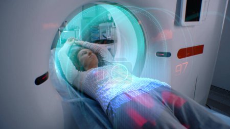 Téléchargez les photos : La femme subit une IRM ou une tomodensitométrie, se trouve sur le lit à l'intérieur de la machine. Animation VFX de scanner le cerveau et le corps de la patiente. Équipement avancé de réalité augmentée dans le laboratoire médical moderne avec Ai - en image libre de droit