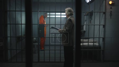 Häftling in orangefarbener Uniform geht hinter Gitter in Gefängniszelle, spricht mit Anwalt, liest Anwaltsvertrag. Verbrecher verbüßt Haftstrafe für Verbrechen im Gefängnis. Haftanstalt oder Justizvollzugsanstalt.