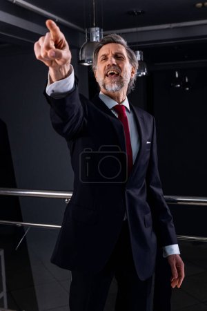 Photo for Positive mature politician comes on press conference with news journalists. Male diplomat or businessman gestures and poses for cameras for media and television live broadcast in government building. - Royalty Free Image