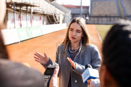 Photo for Two organization representative answer press questions and give interview on a soccer stadium. Interview of successful SEO at press conference for TV news. Crowd of journalists during press campaign. - Royalty Free Image
