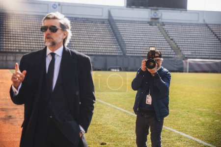 Foto de Un fotógrafo trabaja en una conferencia de prensa en el estadio, fotografiando a un político o al dueño de un club de fútbol. - Imagen libre de derechos