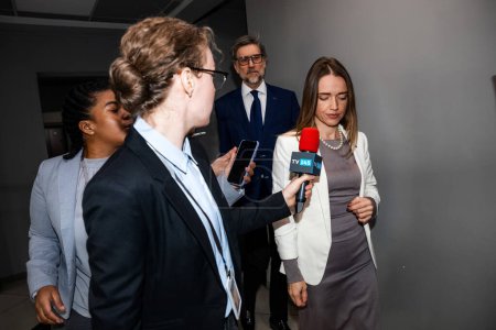 Photo for Positive female EU consul answers press questions and gives interview for media walking in government building corridor. Representative of the European Union surrounded by TV journalists. Press - Royalty Free Image