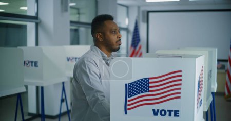 Foto de Hombre afroamericano toma boleta de papel para votar del oficial de votación en el centro de votación. Ciudadano estadounidense camina a la cabina de votación para llenar el boletín. Día de las elecciones en los Estados Unidos de América. Deber cívico. - Imagen libre de derechos