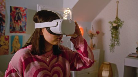 Teenager-Mädchen mit AR-Headset spielt Virtual-Reality-Online-Videospiele in ihrem gemütlichen Schlafzimmer. Mädchen verbringen Freizeit und Spaß zu Hause. Konzept moderner Geräte, Unterhaltung und Lifestyle.
