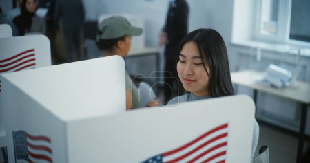 Asian female American citizen votes in booth in polling station office. National Elections Day in the United States. Political races of US presidential candidates. Civic duty and patriotism concept.