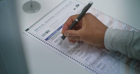 Primer plano del hombre afroamericano anónimo que elige a cuál candidato presidencial votar en papeleta en la cabina de votación. Ciudadano estadounidense en el colegio electoral. Día Nacional de Elecciones en Estados Unidos.