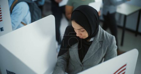 Téléchargez les photos : Une musulmane en hijab vote dans un bureau de vote moderne. Journée nationale des élections aux États-Unis. Courses politiques des candidats à la présidence américaine. Concept de devoir civique et de patriotisme. - en image libre de droit