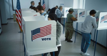 Téléchargez les photos : Une Arabe en hijab vote dans un bureau de vote. Journée nationale des élections aux États-Unis. Courses politiques des candidats à la présidence américaine. Concept de devoir civique et de patriotisme. Dolly shot. - en image libre de droit