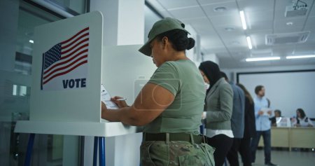Female American army soldier votes in booth in polling station office. National Elections Day in the United States. Political races of US presidential candidates. Concept of civic duty. Dolly shot.