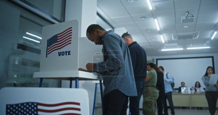 Téléchargez les photos : Un Afro-Américain vote dans un bureau de vote moderne. Journée nationale des élections aux États-Unis. Courses politiques des candidats à la présidence américaine. Concept de patriotisme et devoir civique. - en image libre de droit
