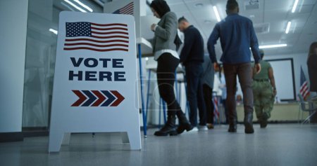 Photo for Vote here sign on the floor. Multi ethnic American citizens vote in booths in polling station office. National Election Day in United States. Political races of US presidential candidates. Civic duty. - Royalty Free Image