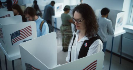 Photo for National Election Day in United States. Woman in glasses votes in booth in polling station office. Political races of US presidential candidates. Civic duty and patriotism. Slow motion. Dolly shot. - Royalty Free Image