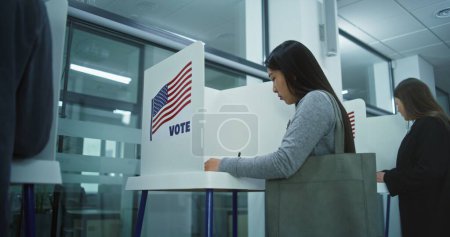 Téléchargez les photos : Une femme asiatique vient aux urnes dans un bureau de vote. Journée nationale des élections aux États-Unis. Courses politiques des candidats à la présidence américaine. Concept de devoir civique et de patriotisme. Dolly shot. - en image libre de droit