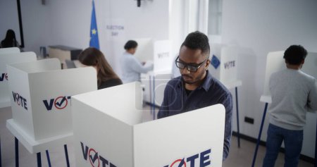 Hoher Anteil multiethnischer Europäer, die während der EU-Wahlen im Wahllokal ihre Stimme abgeben. Verschiedene Wähler füllen Stimmzettel in Wahlkabinen aus. Wahltag in der Europäischen Union. Bürgerpflicht und Demokratie.