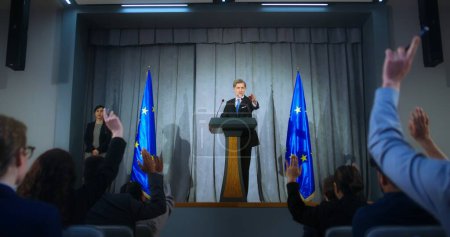 Photo for Confident politician makes an announcement, answers media questions and gives interview. Mature representative of the European Union during performance at press conference. Backdrop with EU flags. - Royalty Free Image