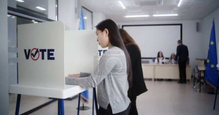 Peuple européen multiethnique votant dans un bureau de vote lors des élections européennes. Divers électeurs remplissent les bulletins de vote dans les isoloirs. Le jour des élections dans l'Union européenne. Devoir civique et démocratie.